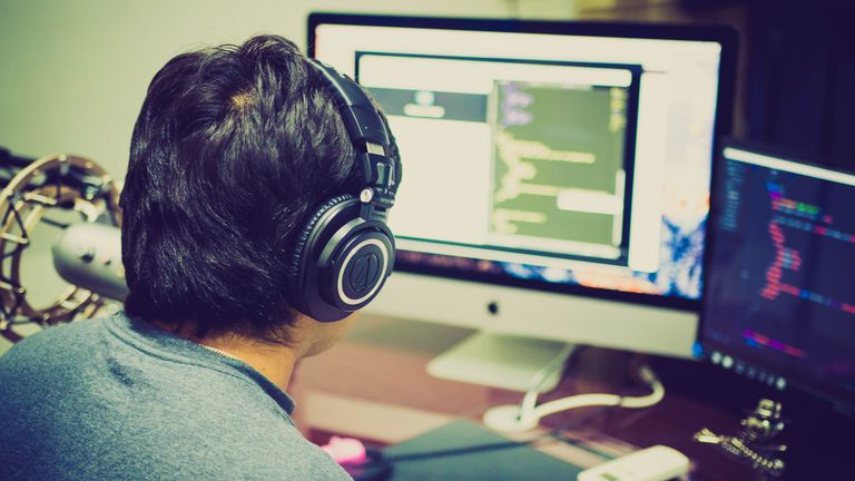 Developer Tools News Today A programmer with headphones focuses on coding at a computer setup with dual monitors.