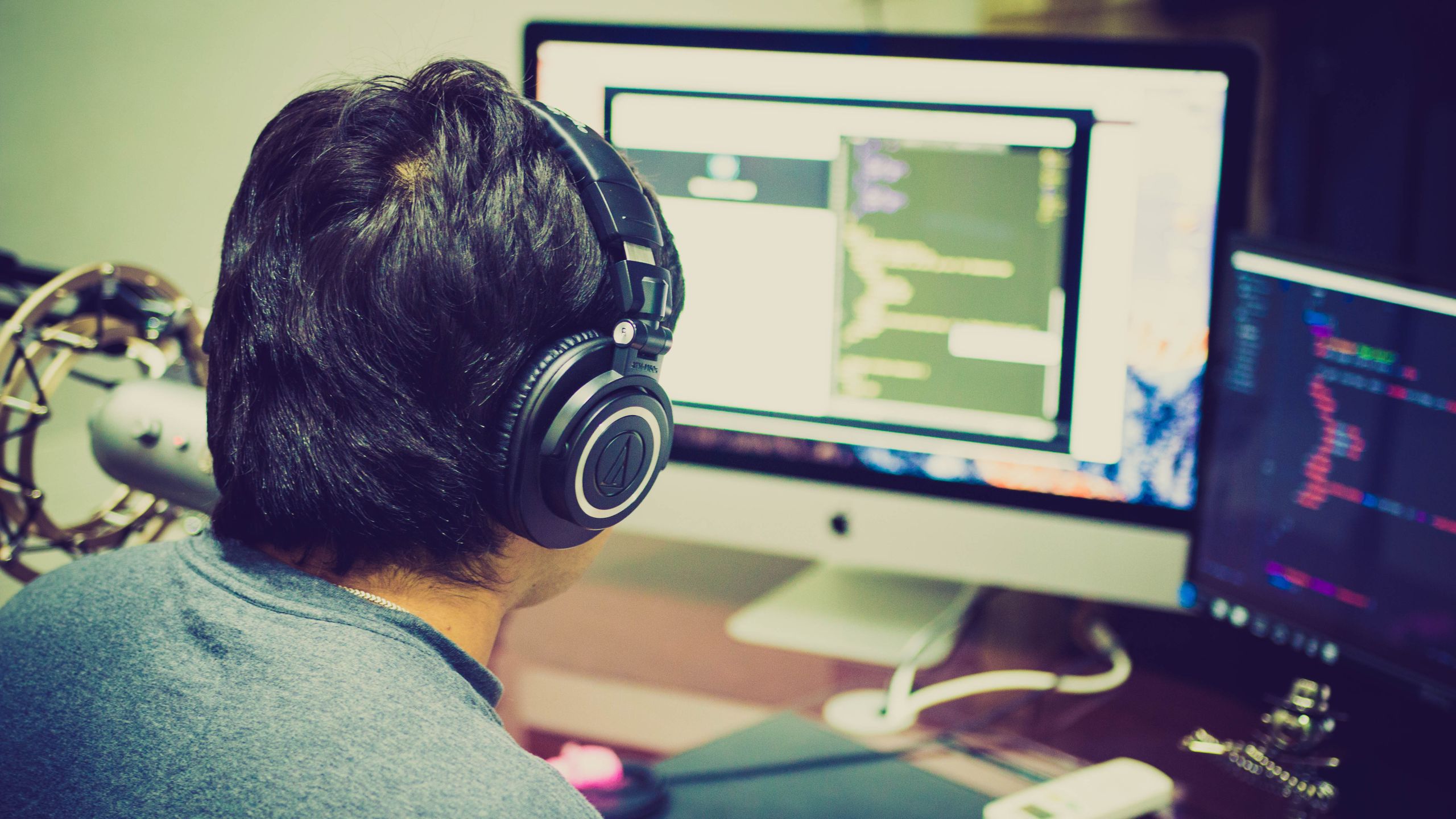 Developer Tools News Today A programmer with headphones focuses on coding at a computer setup with dual monitors.
