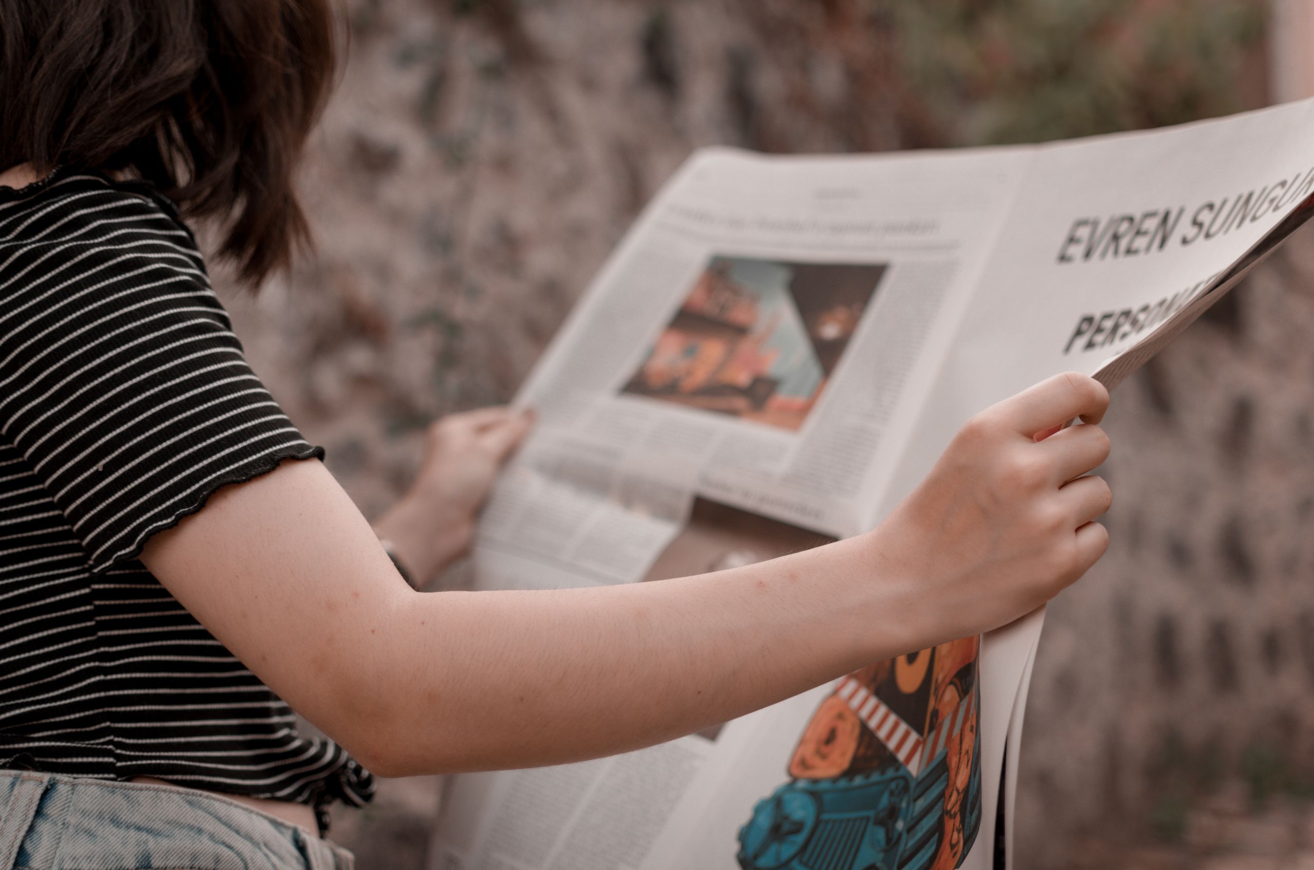 UploadBlog Content A woman holding a newspaper while sitting outside, enjoying a leisurely read.