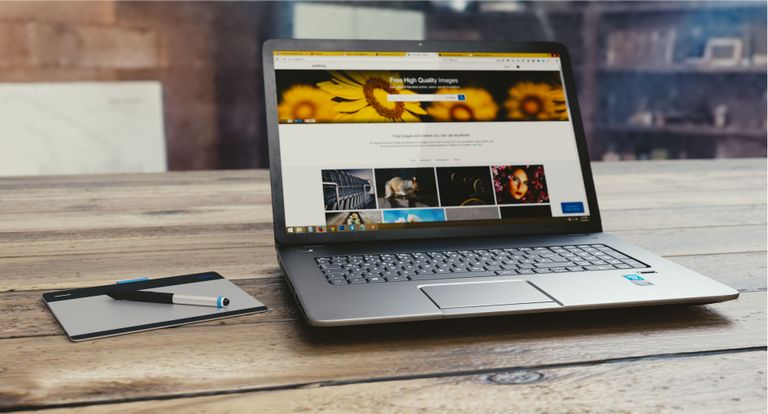 UploadBlog.com Content Marketing Laptop with open webpage on wooden desk, accompanied by tablet and pen, representing digital work setup.