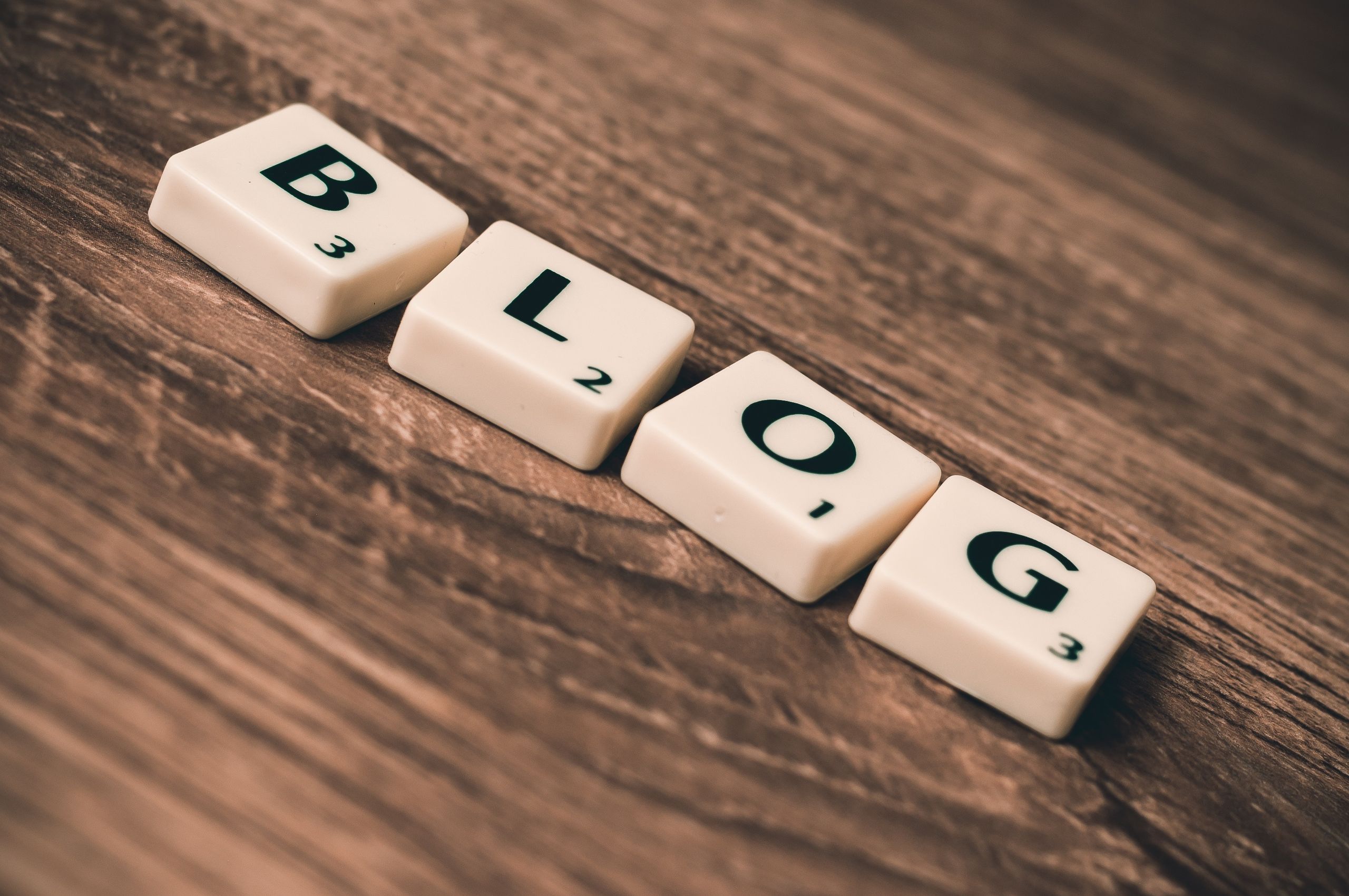 UploadBlog.com Online Posting Scrabble tiles spelling 'BLOG' on a wooden background, symbolizing creativity and writing.